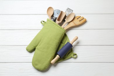 Photo of Different kitchen utensils in oven mitten on white wooden table, top view