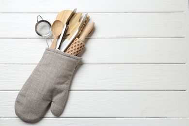 Photo of Different kitchen utensils in oven mitten on white wooden table, top view. Space for text
