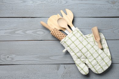 Photo of Different kitchen utensils in oven mitten on light grey wooden table, top view. Space for text
