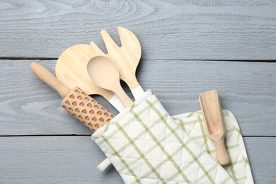 Photo of Different kitchen utensils in oven mitten on light grey wooden table, top view