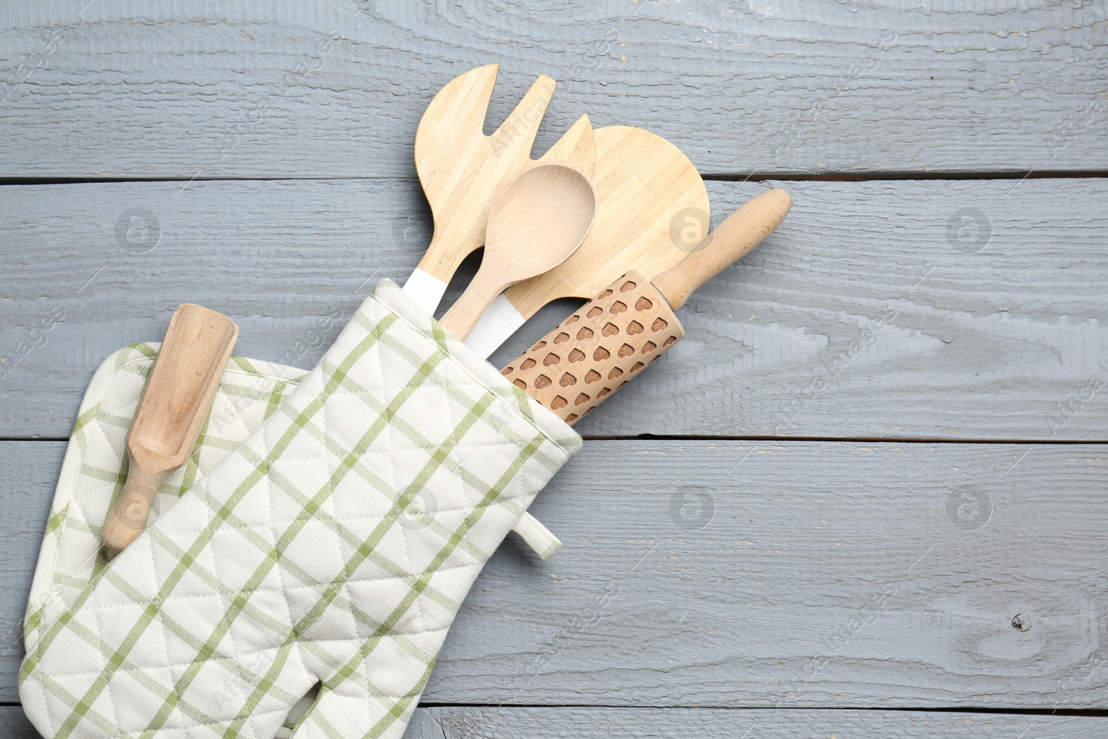 Different kitchen utensils in oven mitten on light grey wooden table, top view. Space for text Photo of Different kitchen utensils in oven mitten on light grey wooden table, top view. Space for text