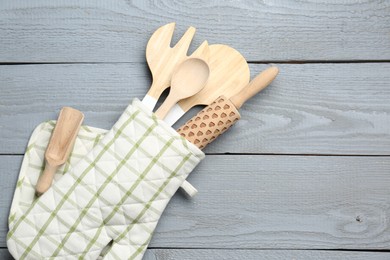 Photo of Different kitchen utensils in oven mitten on light grey wooden table, top view. Space for text