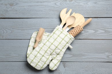 Photo of Different kitchen utensils in oven mitten on light grey wooden table, top view