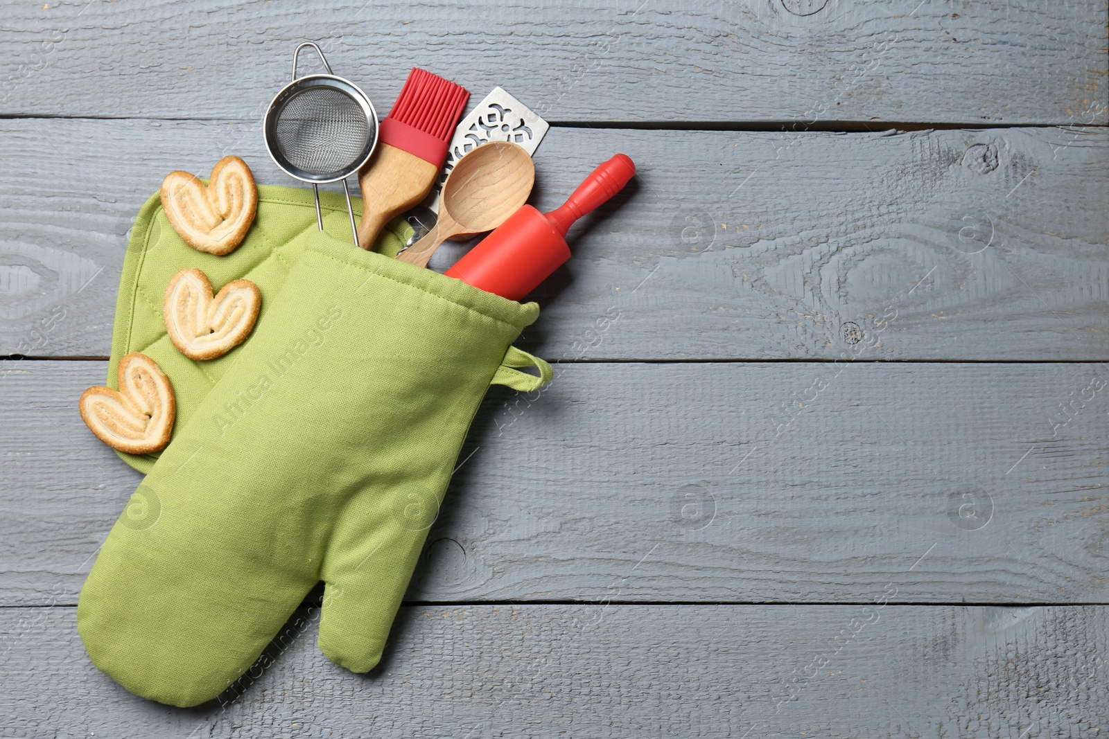 Different kitchen utensils in oven mitten and palmier cookies on light grey wooden table, flat lay. Space for text Photo of Different kitchen utensils in oven mitten and palmier cookies on light grey wooden table, flat lay. Space for text