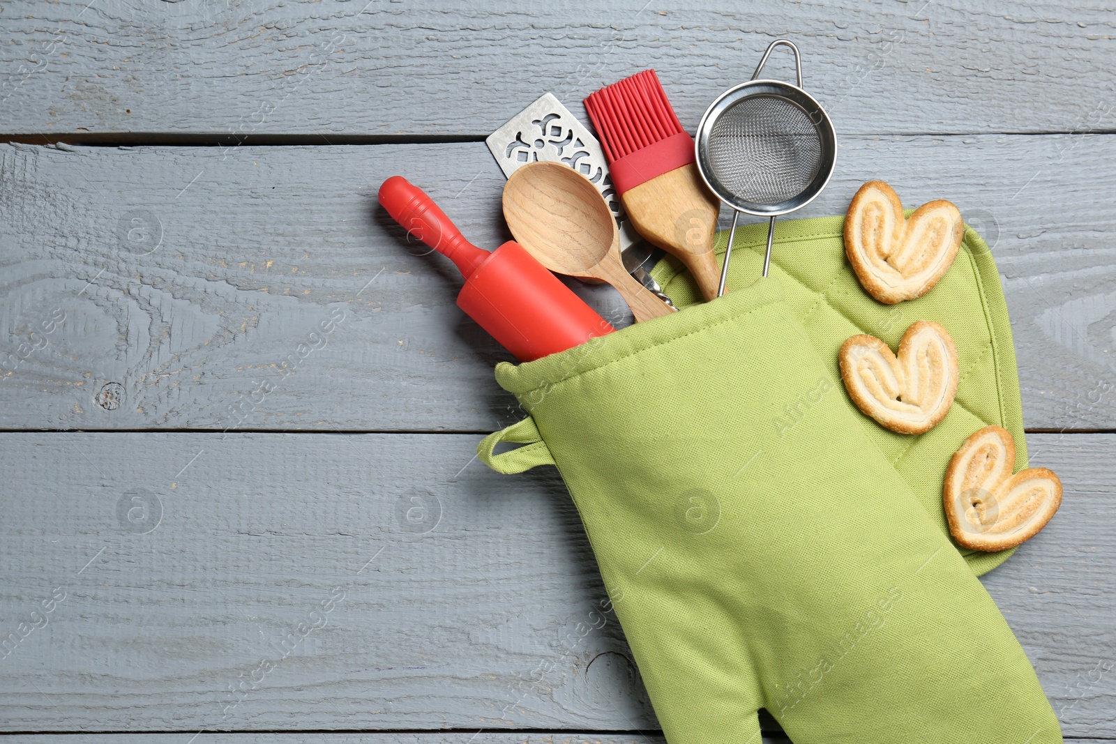 Different kitchen utensils in oven mitten and palmier cookies on light grey wooden table, flat lay. Space for text Photo of Different kitchen utensils in oven mitten and palmier cookies on light grey wooden table, flat lay. Space for text