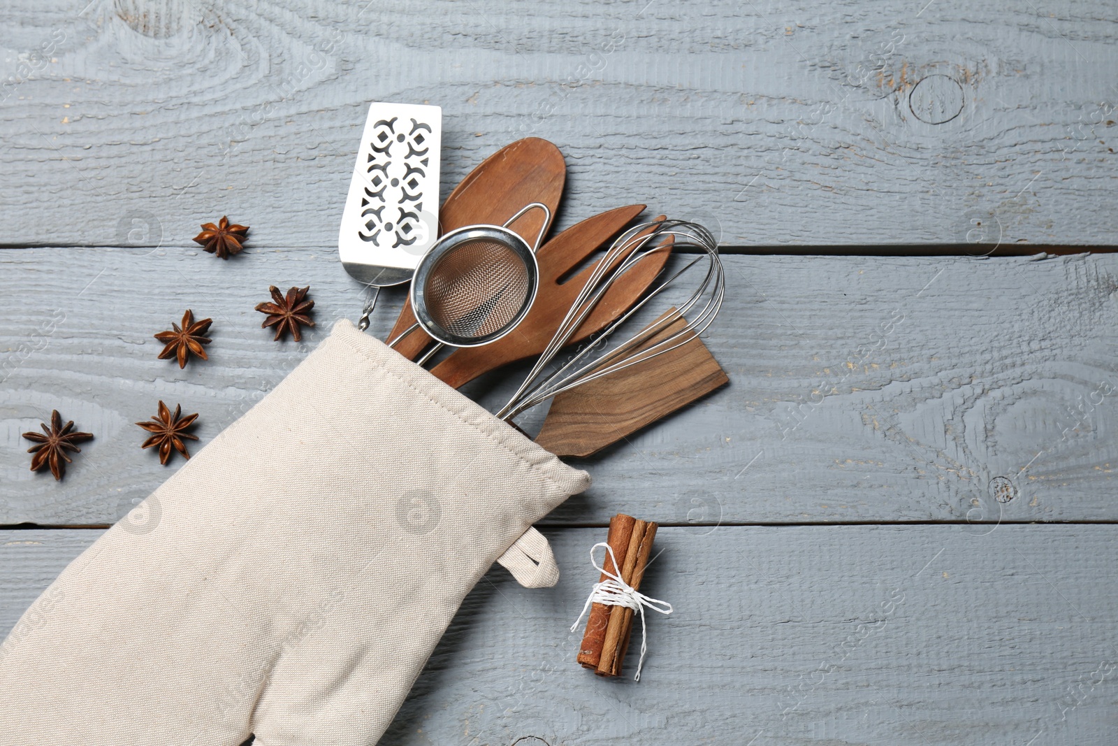 Different kitchen utensils in oven mitten, cinnamon and star anise on light grey wooden table, flat lay. Space for text Photo of Different kitchen utensils in oven mitten, cinnamon and star anise on light grey wooden table, flat lay. Space for text