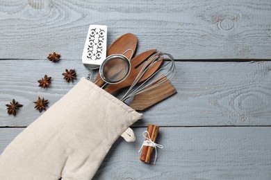 Photo of Different kitchen utensils in oven mitten, cinnamon and star anise on light grey wooden table, flat lay. Space for text