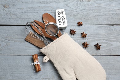 Photo of Different kitchen utensils in oven mitten, cinnamon and star anise on light grey wooden table, flat lay