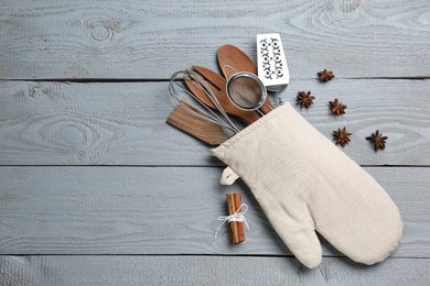 Photo of Different kitchen utensils in oven mitten, cinnamon and star anise on light grey wooden table, flat lay. Space for text