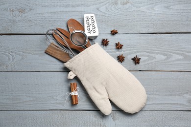Photo of Different kitchen utensils in oven mitten, cinnamon and star anise on light grey wooden table, flat lay