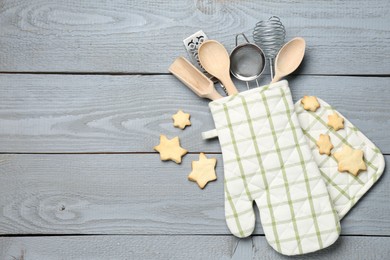 Photo of Different kitchen utensils in oven mitten and star shaped cookies on light grey wooden table, flat lay. Space for text