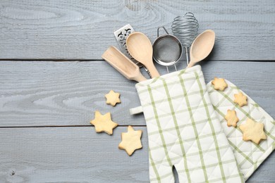 Photo of Different kitchen utensils in oven mitten and star shaped cookies on light grey wooden table, flat lay. Space for text