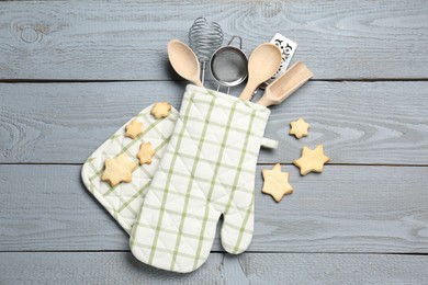 Photo of Different kitchen utensils in oven mitten and star shaped cookies on light grey wooden table, flat lay