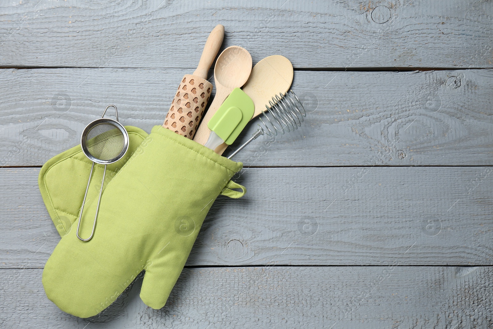 Different kitchen utensils in oven mitten on light grey wooden table, top view. Space for text Photo of Different kitchen utensils in oven mitten on light grey wooden table, top view. Space for text
