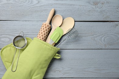 Photo of Different kitchen utensils in oven mitten on light grey wooden table, top view. Space for text