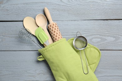 Photo of Different kitchen utensils in oven mitten on light grey wooden table, top view