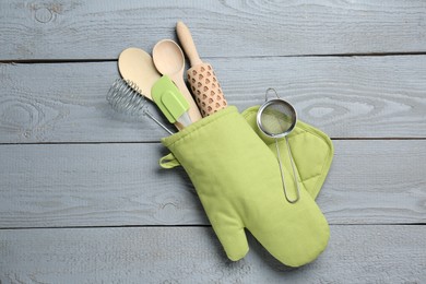 Photo of Different kitchen utensils in oven mitten on light grey wooden table, top view
