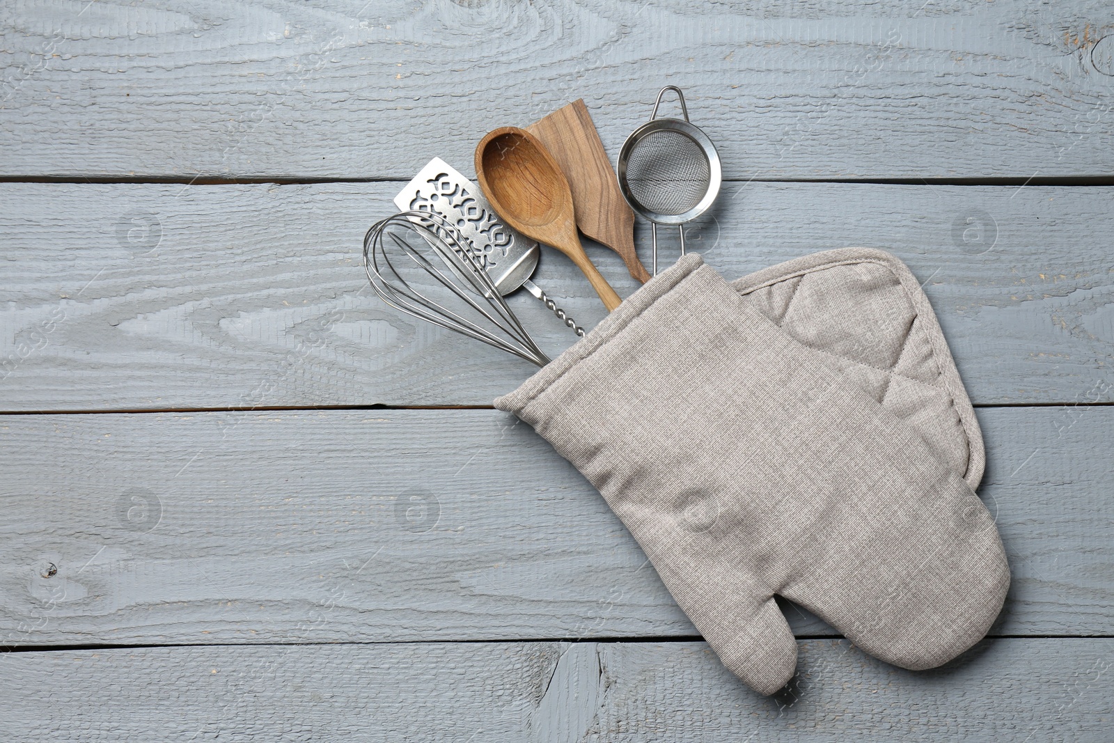 Different kitchen utensils in oven mitten on light grey wooden table, top view. Space for text Photo of Different kitchen utensils in oven mitten on light grey wooden table, top view. Space for text
