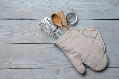 Photo of Different kitchen utensils in oven mitten on light grey wooden table, top view. Space for text