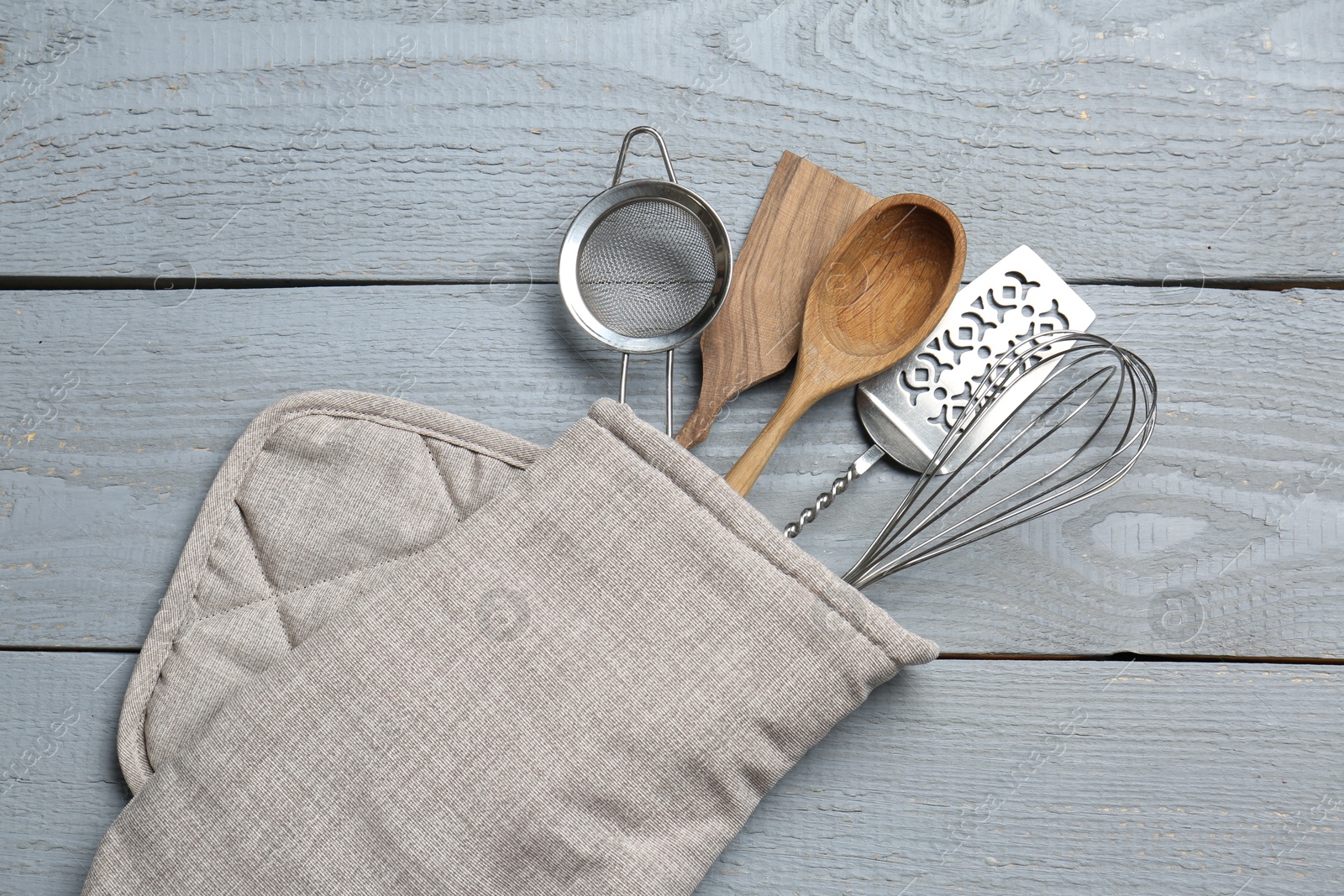 Different kitchen utensils in oven mitten on light grey wooden table, top view Photo of Different kitchen utensils in oven mitten on light grey wooden table, top view