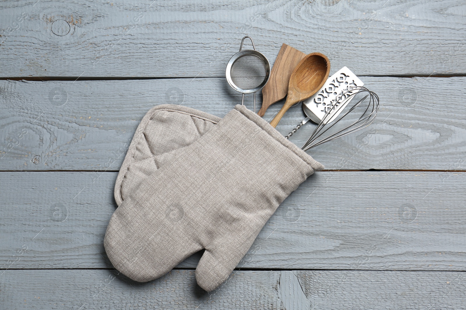 Different kitchen utensils in oven mitten on light grey wooden table, top view Photo of Different kitchen utensils in oven mitten on light grey wooden table, top view