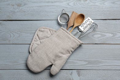 Photo of Different kitchen utensils in oven mitten on light grey wooden table, top view