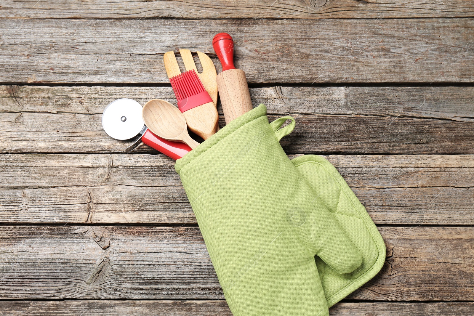 Different kitchen utensils in oven mitten on wooden table, top view Photo of Different kitchen utensils in oven mitten on wooden table, top view