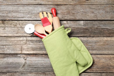 Photo of Different kitchen utensils in oven mitten on wooden table, top view
