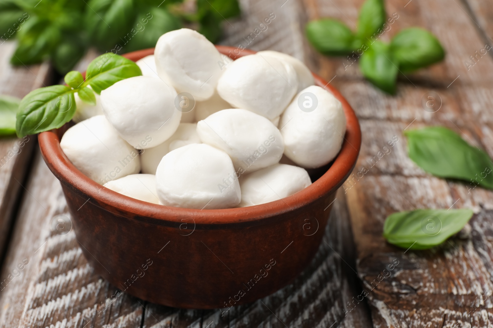 Tasty mozzarella cheese balls in bowl and basil on wooden table, closeup Photo of Tasty mozzarella cheese balls in bowl and basil on wooden table, closeup