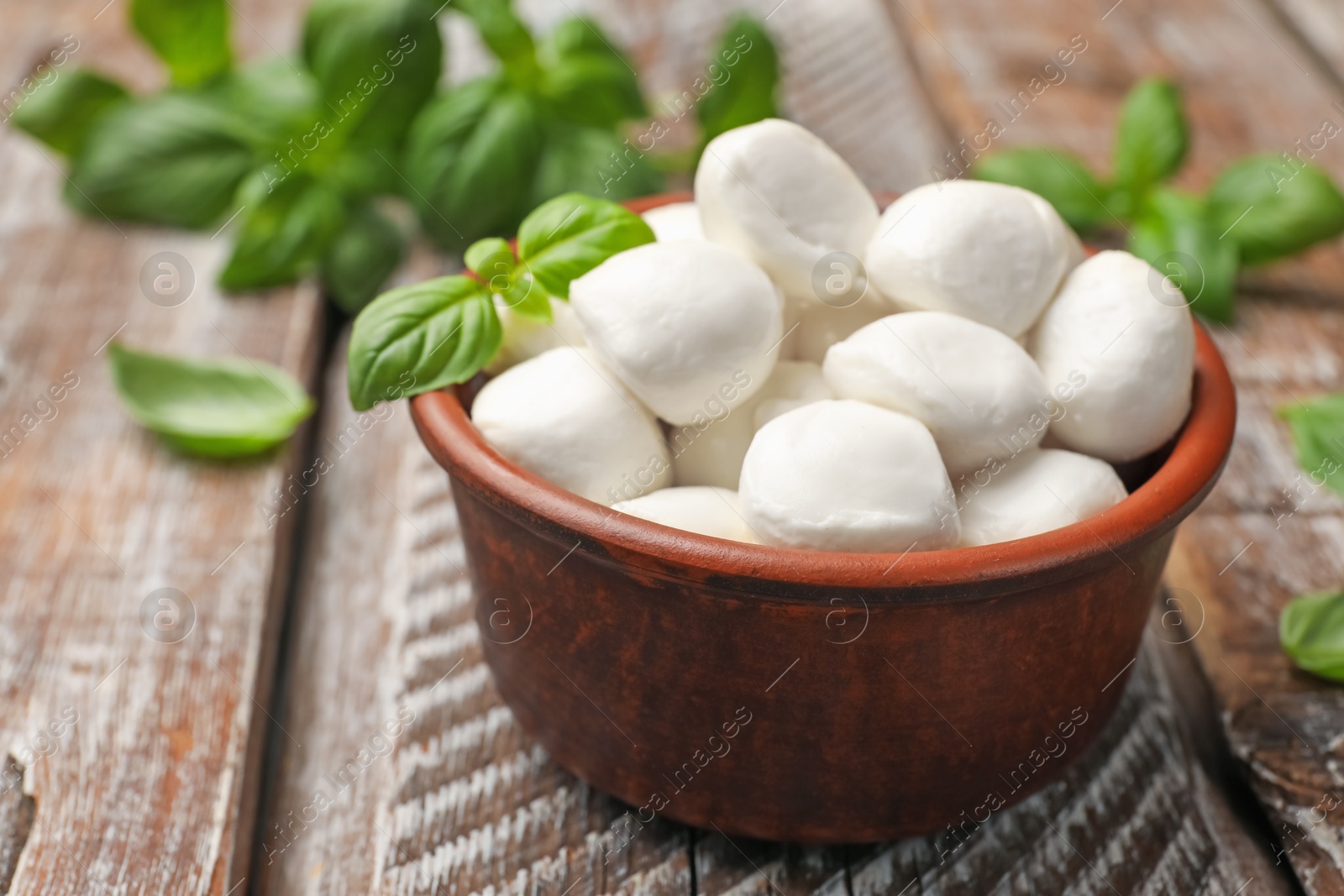 Tasty mozzarella cheese balls in bowl and basil on wooden table, closeup Photo of Tasty mozzarella cheese balls in bowl and basil on wooden table, closeup