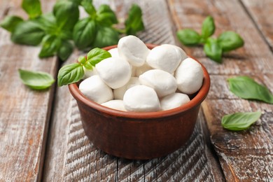 Photo of Tasty mozzarella cheese balls in bowl and basil on wooden table, closeup
