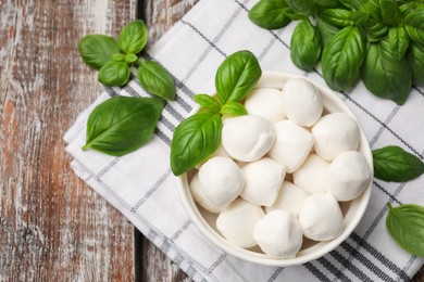 Photo of Tasty mozzarella cheese balls in bowl and basil on wooden table, flat lay. Space for text