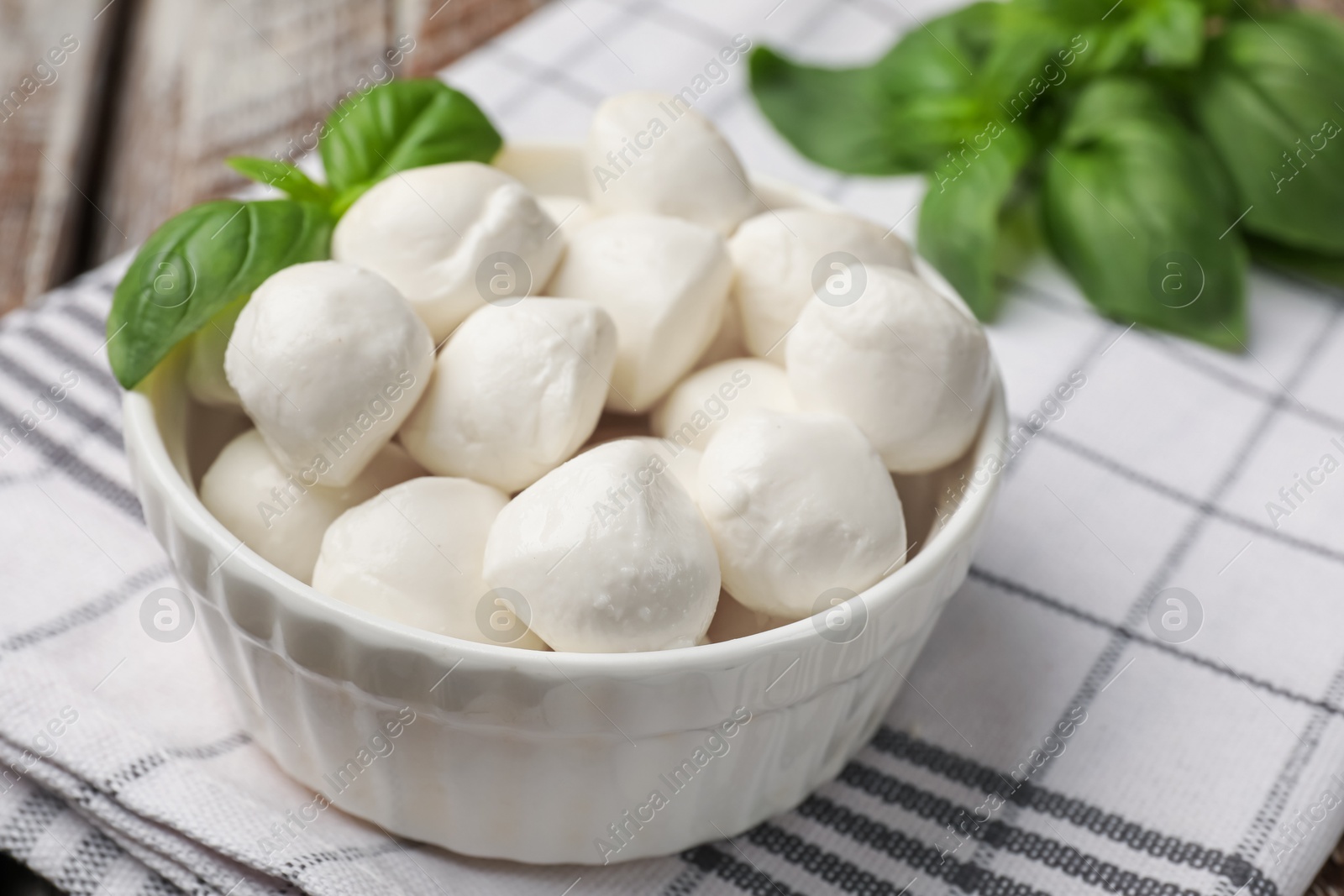 Tasty mozzarella cheese balls in bowl and basil on table, closeup Photo of Tasty mozzarella cheese balls in bowl and basil on table, closeup