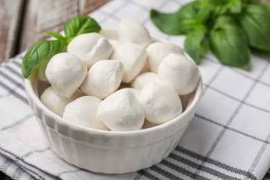 Photo of Tasty mozzarella cheese balls in bowl and basil on table, closeup