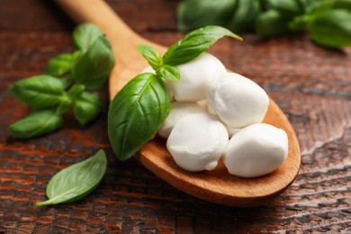 Photo of Tasty mozzarella cheese balls in spoon and basil on wooden table, closeup
