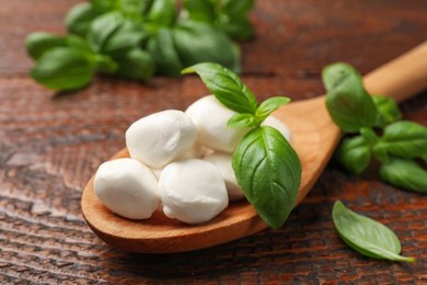 Photo of Tasty mozzarella cheese balls in spoon and basil on wooden table, closeup