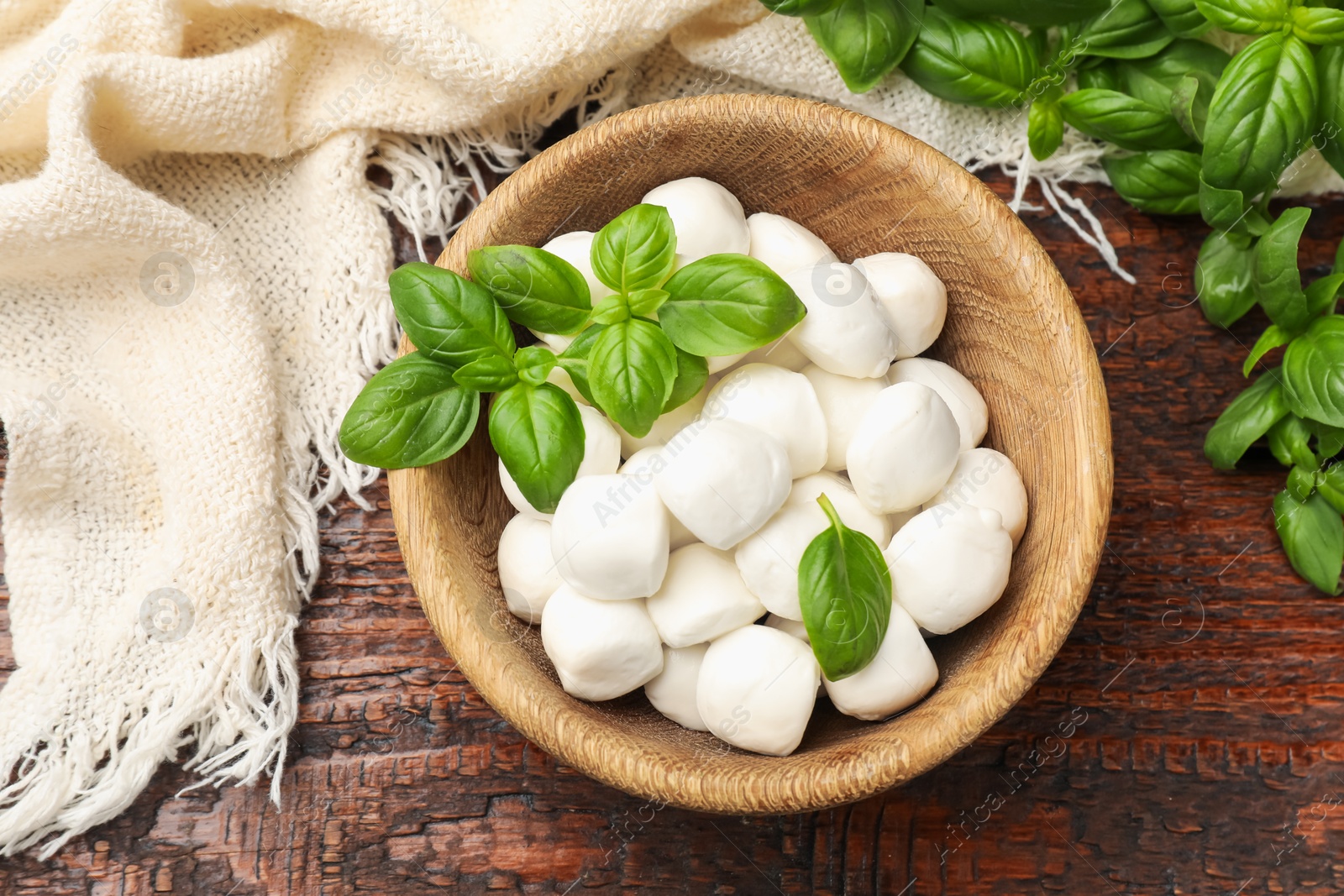 Tasty mozzarella cheese balls in bowl and basil on wooden table, flat lay Photo of Tasty mozzarella cheese balls in bowl and basil on wooden table, flat lay