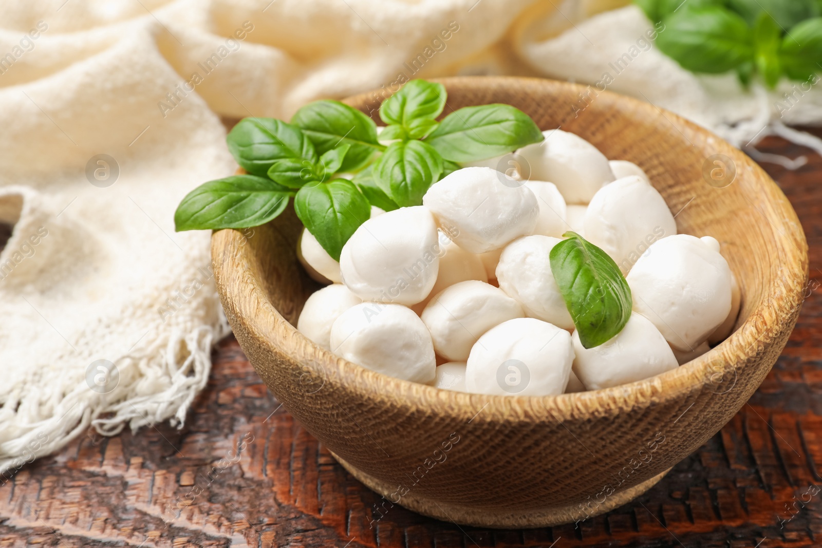 Tasty mozzarella cheese balls in bowl and basil on wooden table, closeup Photo of Tasty mozzarella cheese balls in bowl and basil on wooden table, closeup