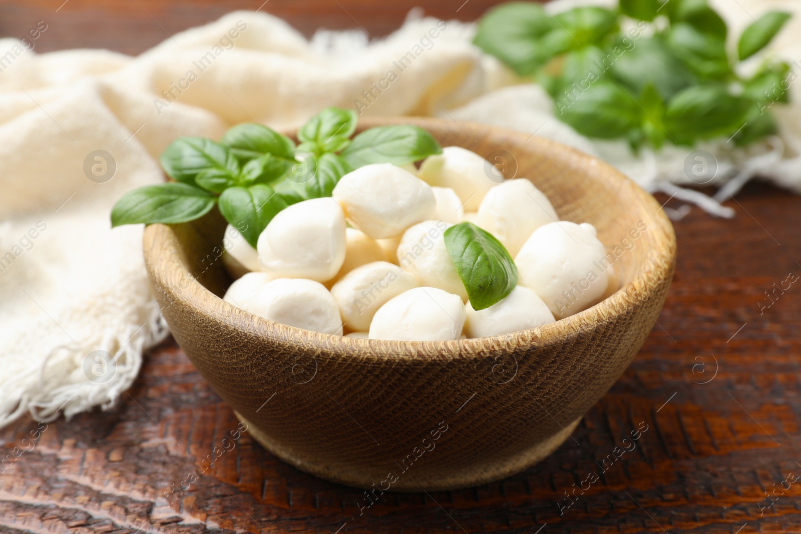 Tasty mozzarella cheese balls in bowl and basil on wooden table, closeup Photo of Tasty mozzarella cheese balls in bowl and basil on wooden table, closeup
