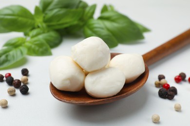 Photo of Tasty mozzarella cheese balls in spoon, basil and peppercorns on white marble table, closeup