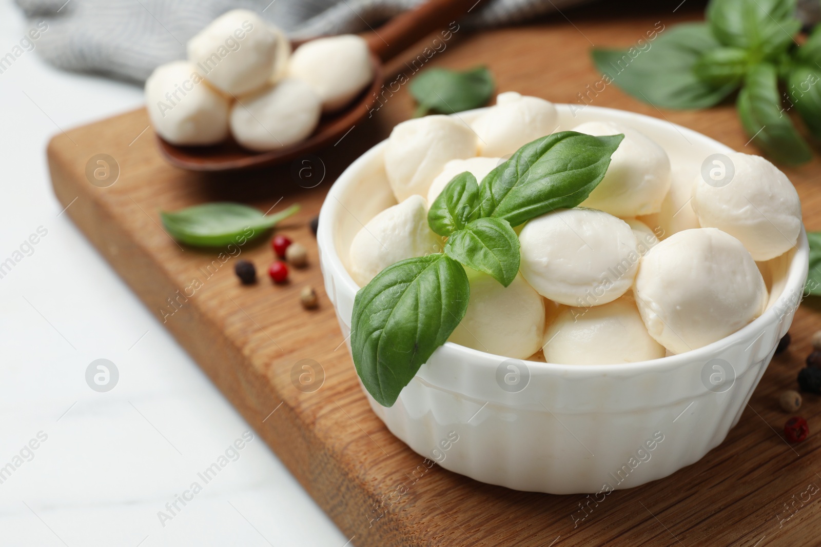 Tasty mozzarella cheese balls in bowl, spoon, basil and peppercorns on white marble table, closeup Photo of Tasty mozzarella cheese balls in bowl, spoon, basil and peppercorns on white marble table, closeup