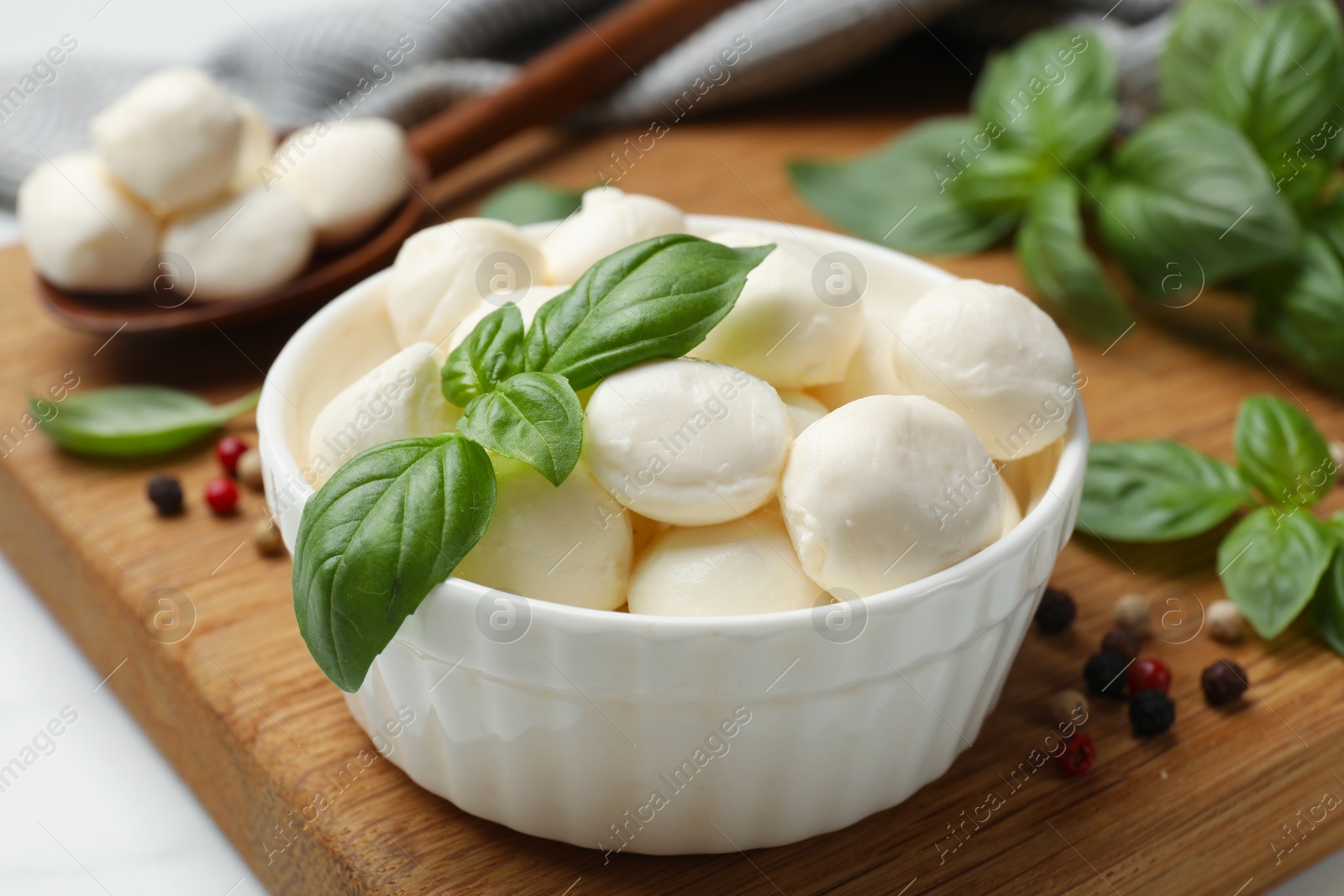 Tasty mozzarella cheese balls in bowl, spoon, basil and peppercorns on white table, closeup Photo of Tasty mozzarella cheese balls in bowl, spoon, basil and peppercorns on white table, closeup