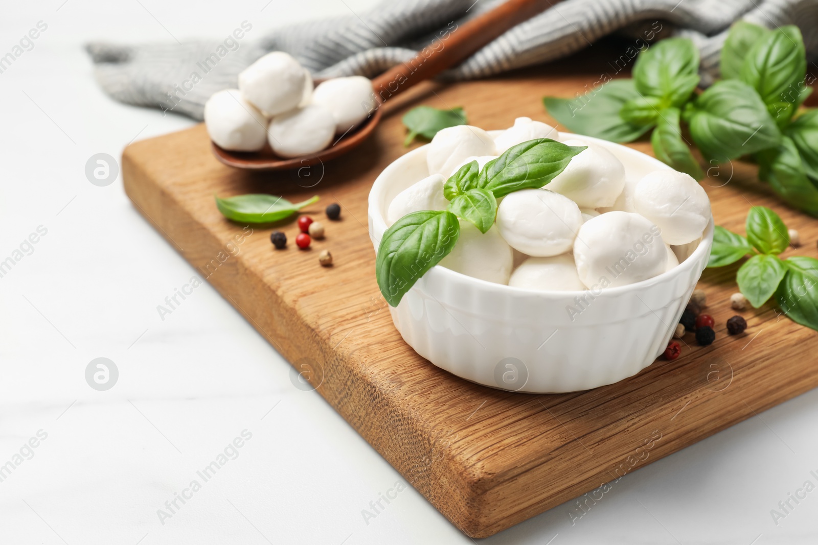 Tasty mozzarella cheese balls in bowl, spoon, basil and peppercorns on white marble table, closeup Photo of Tasty mozzarella cheese balls in bowl, spoon, basil and peppercorns on white marble table, closeup