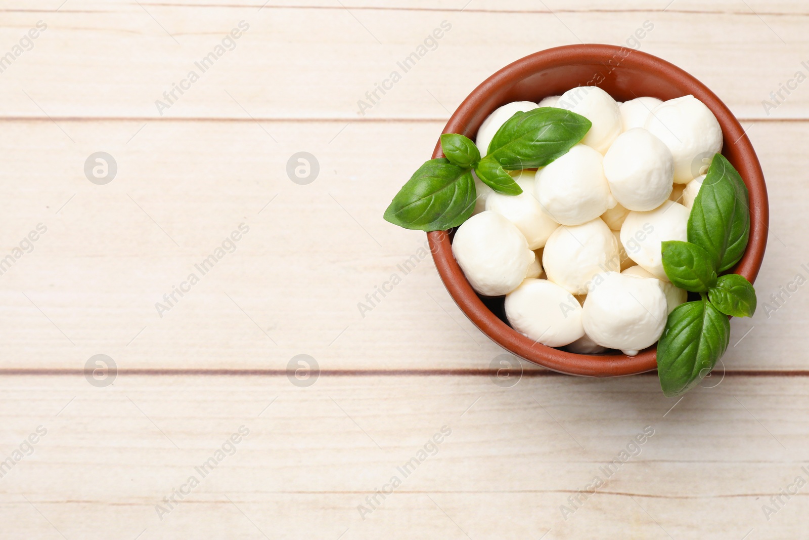 Tasty mozzarella cheese balls in bowl and basil on light wooden table, top view. Space for text Photo of Tasty mozzarella cheese balls in bowl and basil on light wooden table, top view. Space for text