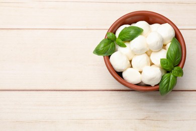 Photo of Tasty mozzarella cheese balls in bowl and basil on light wooden table, top view. Space for text