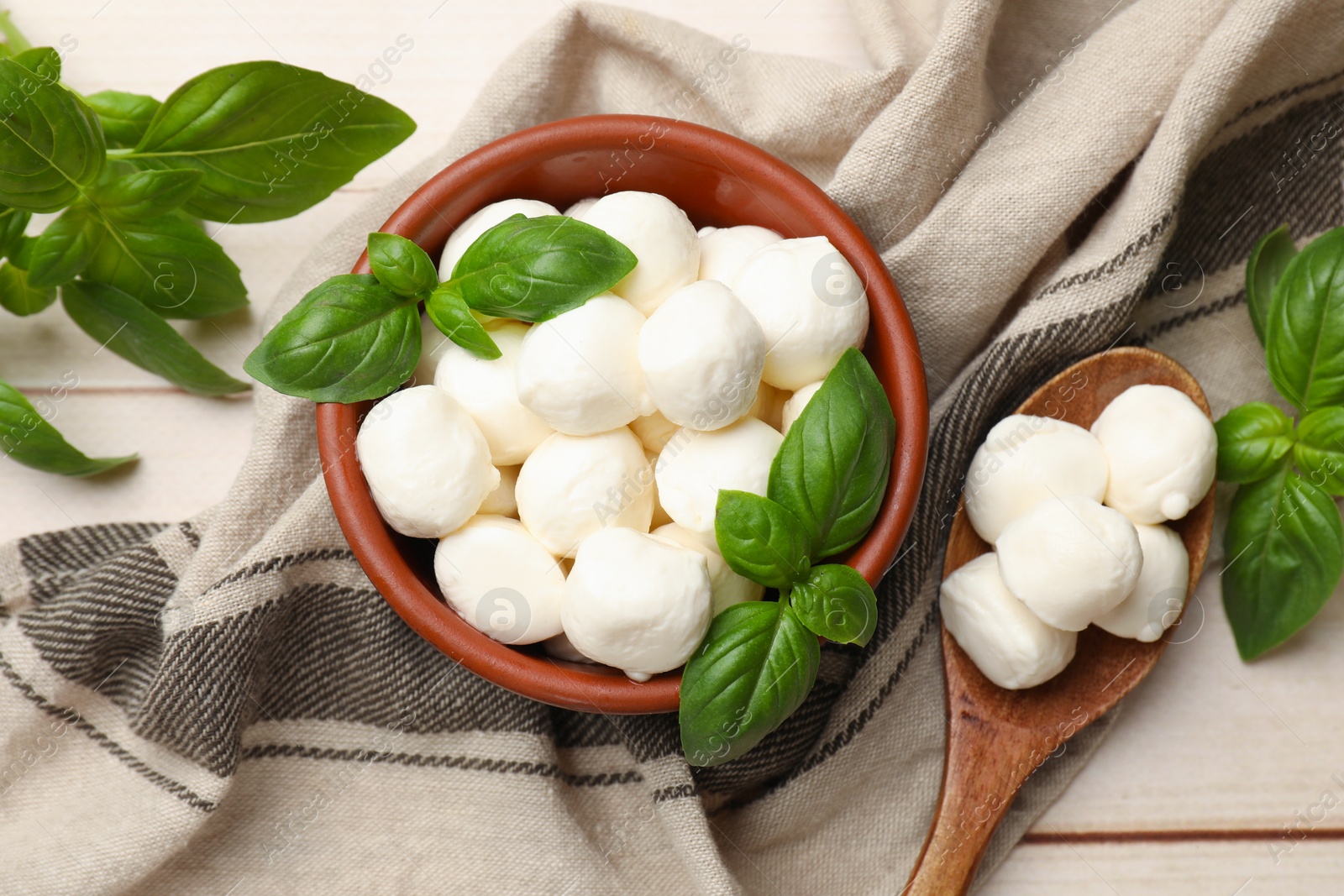Tasty mozzarella cheese balls in bowl, basil and spoon on light wooden table, flat lay Photo of Tasty mozzarella cheese balls in bowl, basil and spoon on light wooden table, flat lay
