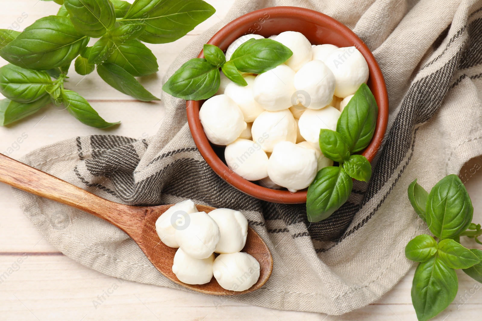 Tasty mozzarella cheese balls in bowl, basil and spoon on light wooden table, flat lay Photo of Tasty mozzarella cheese balls in bowl, basil and spoon on light wooden table, flat lay