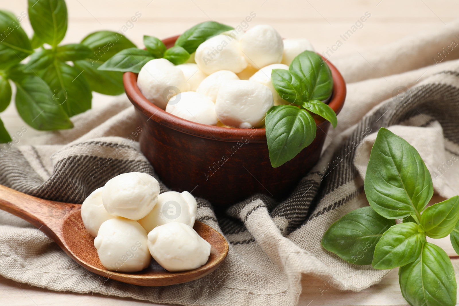 Tasty mozzarella cheese balls in bowl, basil and spoon on light wooden table, closeup Photo of Tasty mozzarella cheese balls in bowl, basil and spoon on light wooden table, closeup
