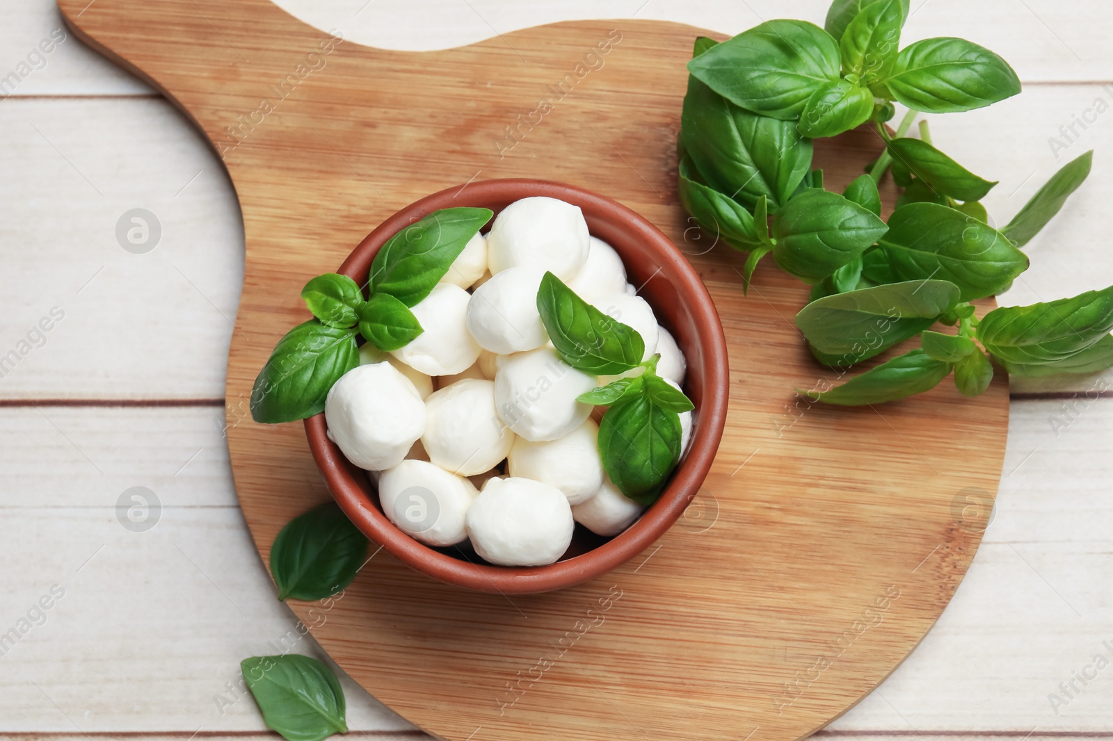 Tasty mozzarella cheese balls in bowl and basil on light wooden table, flat lay Photo of Tasty mozzarella cheese balls in bowl and basil on light wooden table, flat lay