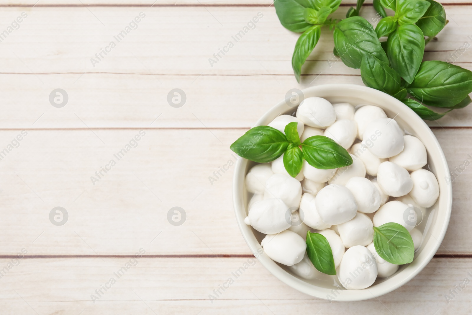 Tasty mozzarella cheese balls in bowl and basil on light wooden table, flat lay. Space for text Photo of Tasty mozzarella cheese balls in bowl and basil on light wooden table, flat lay. Space for text